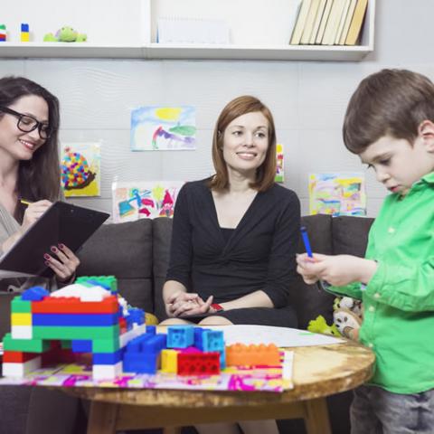 Two women working with and evaluating a child who is playing with blocks on a table